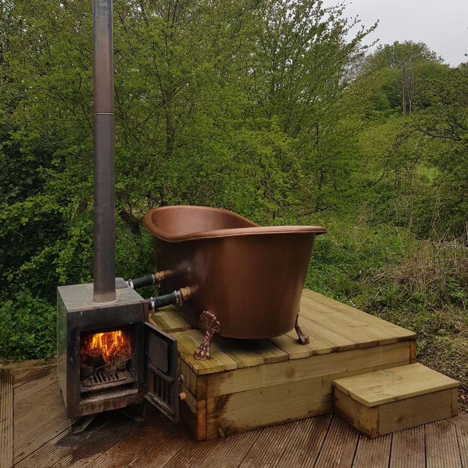 Coppersmith Creations Hammered Clawfoot Copper Double Slipper Tub installed outside with log burner